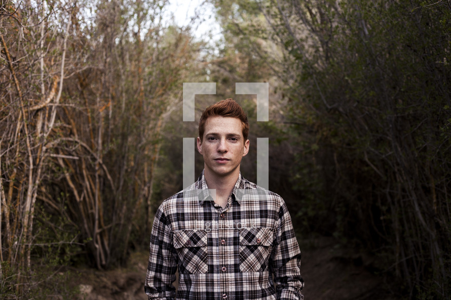 young man with red hair standing outdoors in a plaid shirt 