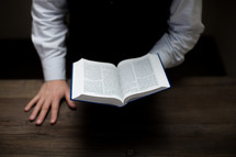 man leaning over a table reading a Bible 