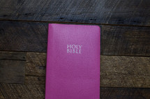 A bright pink Bible on a wooden table.
