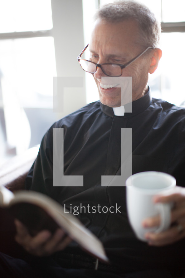 A smiling minister reading the Bible and holding a cup of coffee.