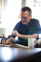 A minister wearing clerical clothes takes notes at a coffee table.