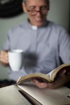 A smiling minister reading the Bible and drinking coffee.