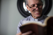 A smiling minister in a clerical reading the Bible.