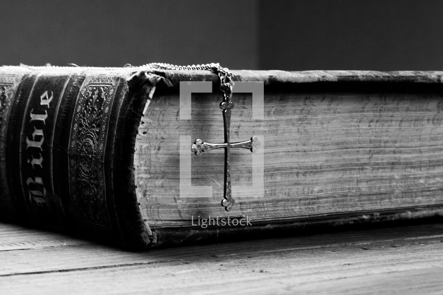 A metal cross on a chain hanging over the edge of an old Bible.