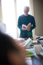A man standing at a table leading a small group in a Bible study.