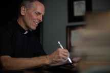 A minister wearing a clerical collar taking notes at a desk.