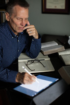 A middle-aged man at a desk with Bible, notebook and electronic pad.
