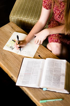 A girl writing notes in a journal while reading a Bible 