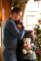 couple hugging with a teddy bear in front of a Christmas tree, Christmas sadness 