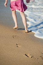 girl child walking leaving footprints in the sand on a beach 