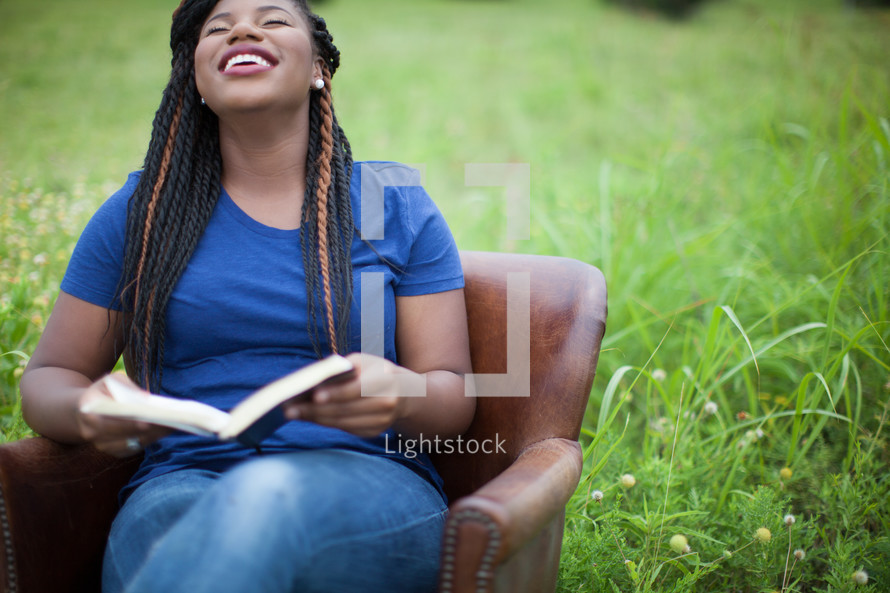 woman sitting in a chair outdoors reading a Bible 
