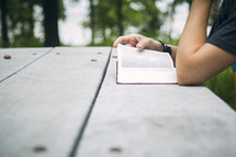 A woman sitting at a picnic table reading the Bible.