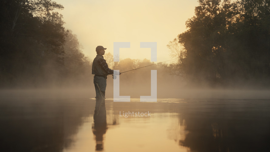 Young fly fisherman casting on a foggy river at sunrise