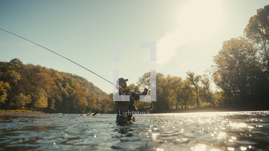 Young fly fisherman casting on a foggy river at sunrise