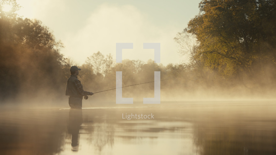 Young fly fisherman casting on a foggy river at sunrise