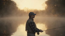 Young fly fisherman casting on a foggy river at sunrise