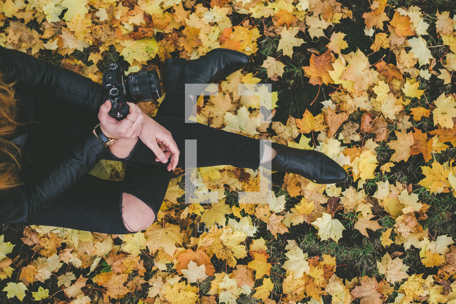 A woman with a camera sitting in fall leaves.