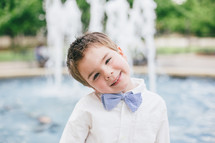 a boy child in a bow tie in front of a fountain 