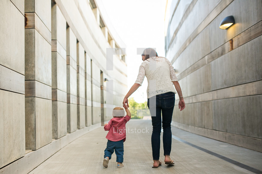 a mother walking holding hands with her toddler 