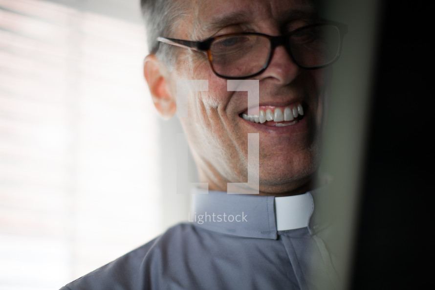 A smiling minister in a clerical collar and glasses.