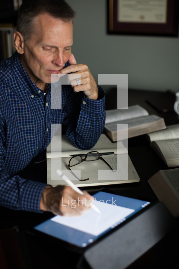 A middle-aged man at a desk with Bible, notebook and electronic pad.