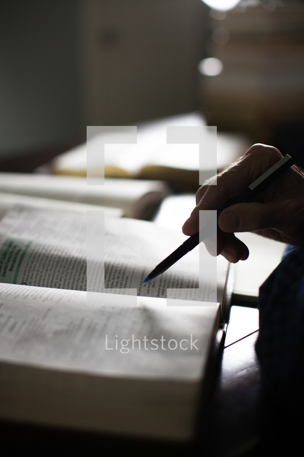 A hand holding a pen over an open Bible.
