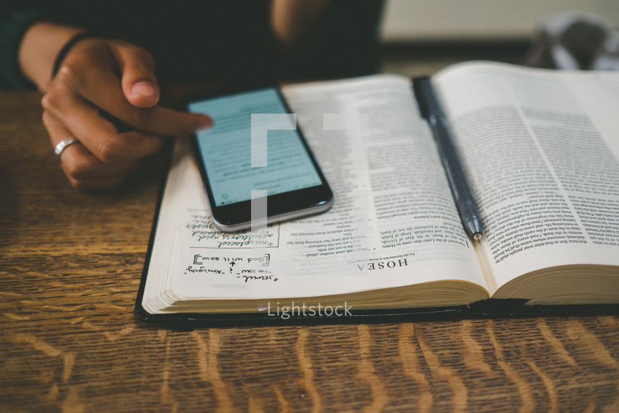 open Bible, notes, pen, and Bible app on a cellphone 