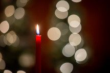 One red melting wax candle burning in front of blurred bokeh Christmas lights