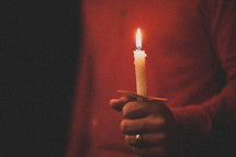 A man wearing a red shirt holding a candle