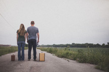man and woman standing with suitcases looking down a long open road