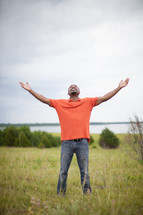 man with open arms standing outdoors in a field 