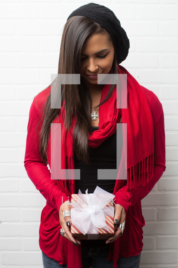 An African-American woman holding a wrapped Christmas gift with her head bowed in prayer 
