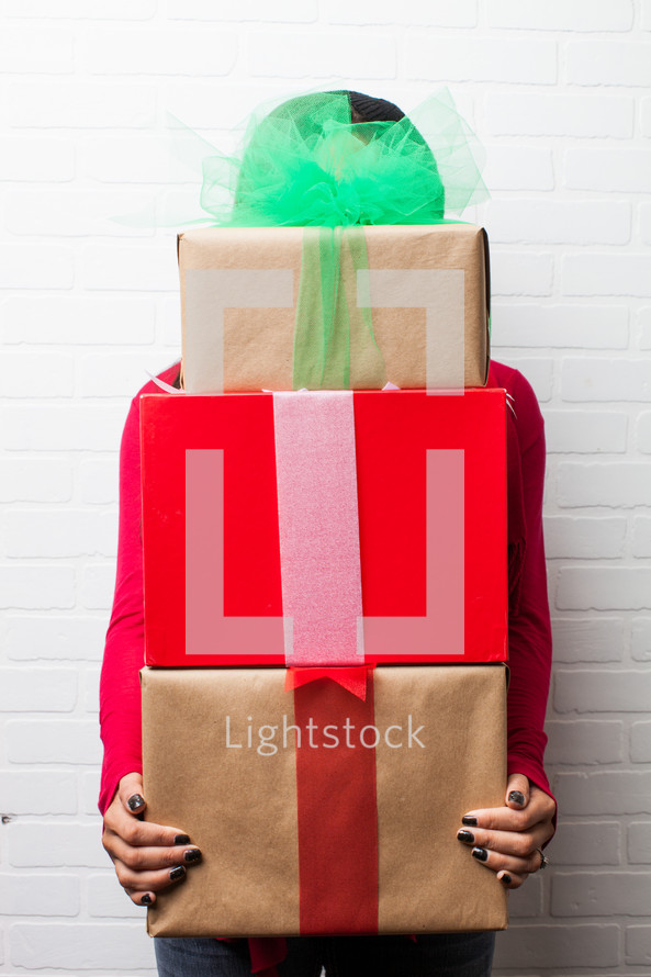a woman holding wrapped gifts towering over her head 
