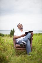 man reading a Bible in a chair outdoors 