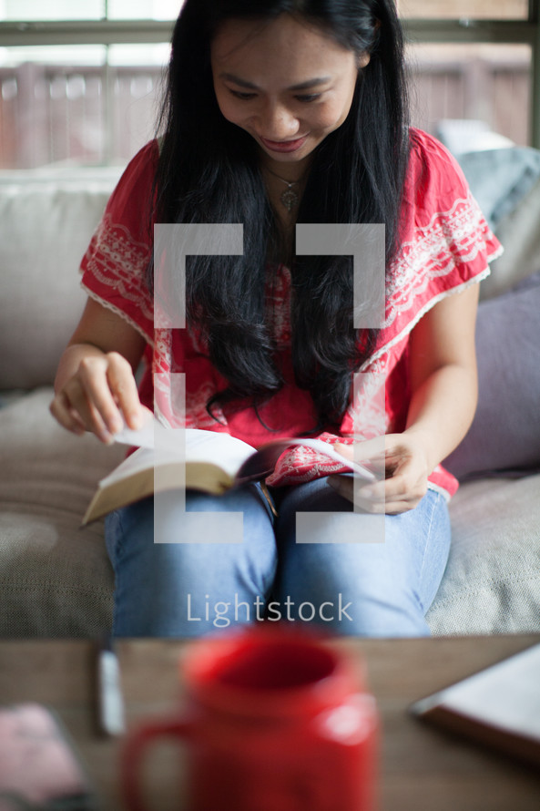 Asian woman reading a Bible on her couch 