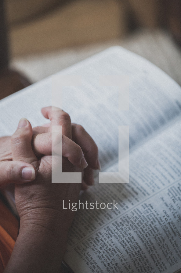 Hands clasped on an open Bible's pages.