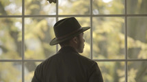 a man in a hat looking out a window 