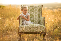 young girl in pigtails sitting in chair in a field