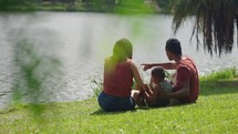 back view of Little boy sitting with father and mother over the lake at city park. Family outdoors, happy parenting and childhood, kids and parents relaxing outside
