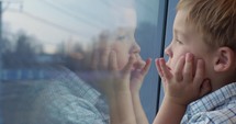 Boy looking out the train window with hands on the face