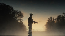 Young fly fisherman casting on a foggy river at sunrise