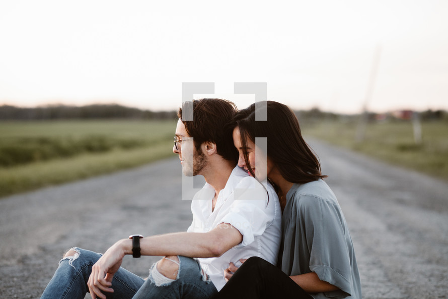 couple snuggling sitting on a dirt road 