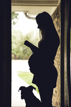 silhouette of a pregnant woman reading a Bible and a dog 