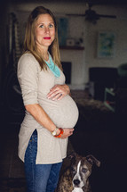 a pregnant woman holding her belly and her pet dog 