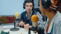 Young man in headphones talking on microphone, having discussion with female co-host, recording podcast in studio. Rack focus shot