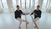 Young graceful ballerina holding one leg on barre, performing backbend and side stretch while exercising in a dance studio with a mirror wall. High angle view
