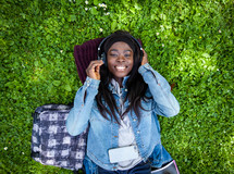 woman lying on green grass listening to music with headphones.