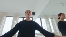 Young talented ballerina doing passe on demi pointe, taking one arm off the barre and keeping a balance while practicing in a dance studio. Tilt-up shot, low angle
