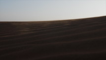 Wind blowing sand and dust over middle eastern desert sand dunes in United Arab Emirates landscape during evening sunset in cinematic slow motion.