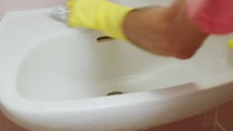 A man's hand cleaning a bathroom sink with brush